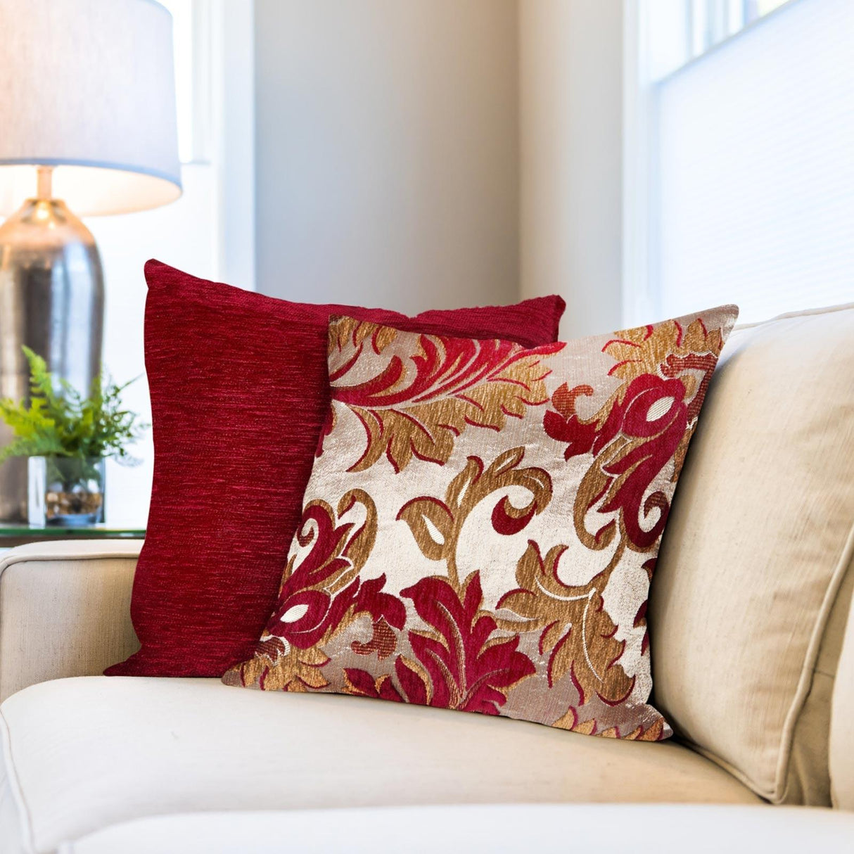 A red and gold damask style chenille cushion cover on a beige sofa with other cushions.