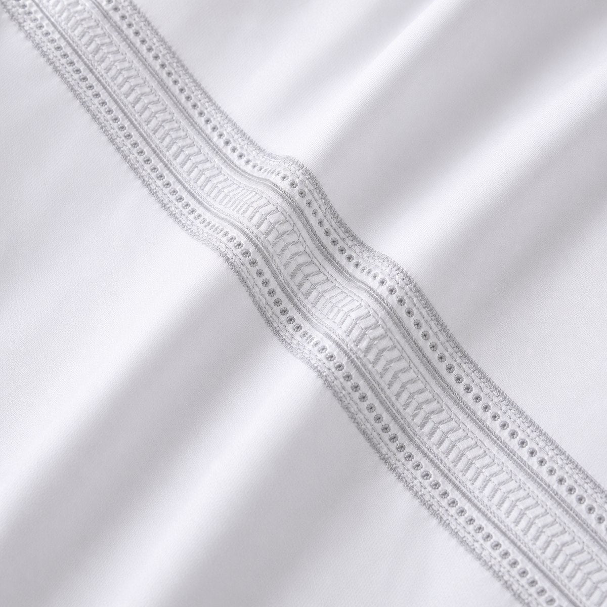 Macro close-up of white cotton fabric with the silver embroidered ladder band detail
