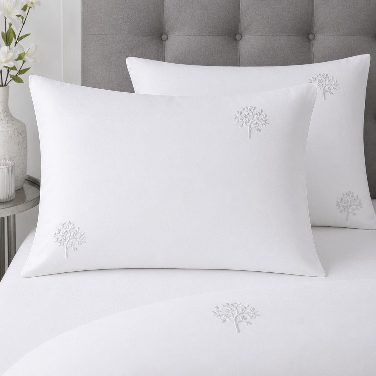 Close-up of white cotton pillowcases with delicate grey embroidered tree motifs