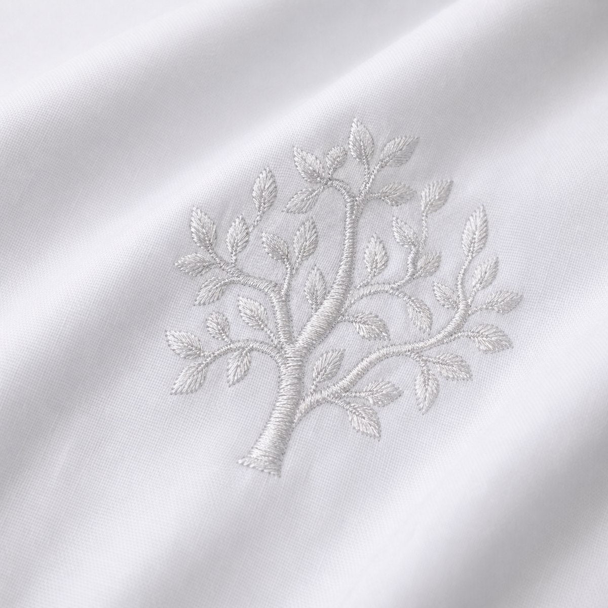 Macro close-up of white cotton fabric with raised grey embroidered tree detail