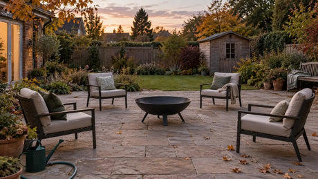 Unlit fire pit on an open stone patio with seating moved back and a hose ready