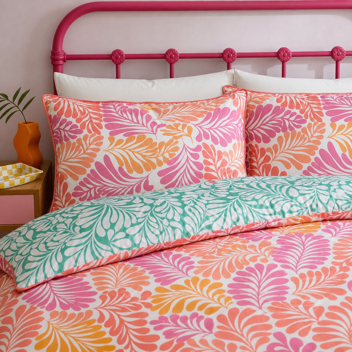 Close-up of Carmen Pink cotton pillowcases with coral leaf print and teal reverse duvet detail
