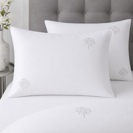 Close-up of white cotton pillowcases with delicate grey embroidered tree motifs